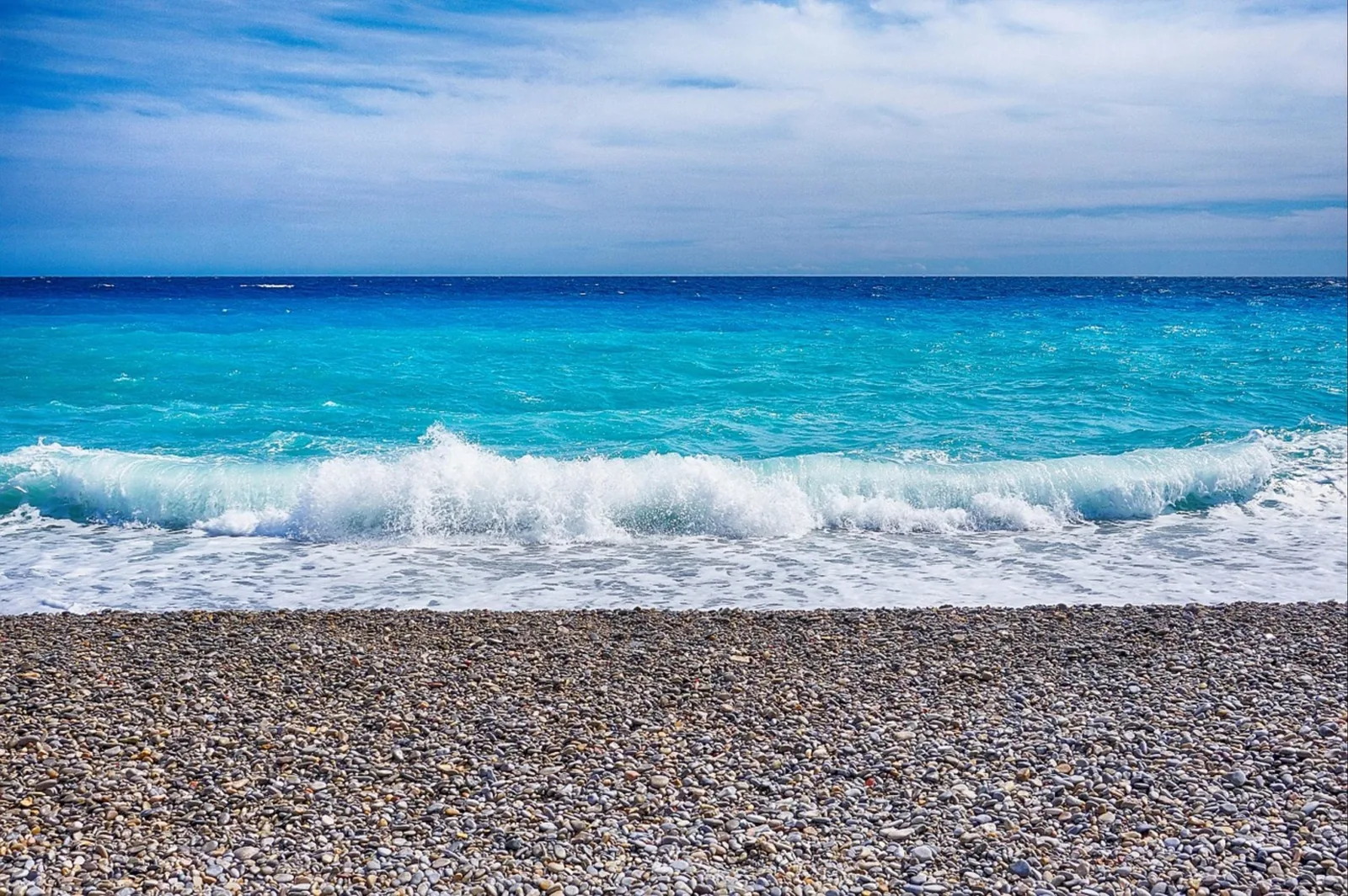 Plage de galets et mer turquoise de la Côte d’Azur, vague et ciel bleu