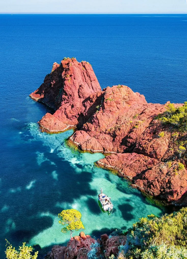 Bateau a l'ancre dans une crique de l'Esterel aux eaux turquoise cernee de roches rouges