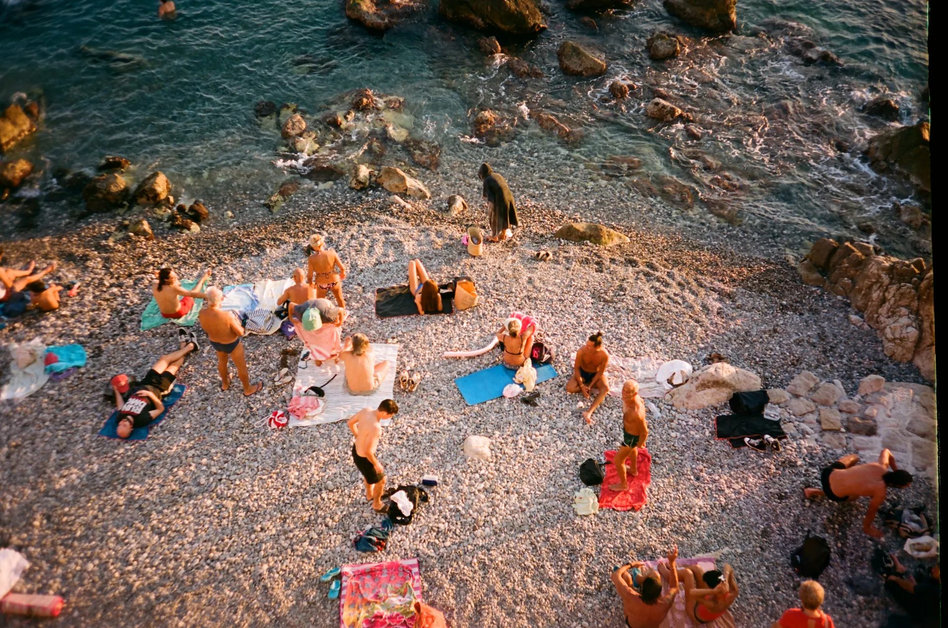 Les baigneurs sur les galets d'une crique du Cap de Nice à la lumière du soir