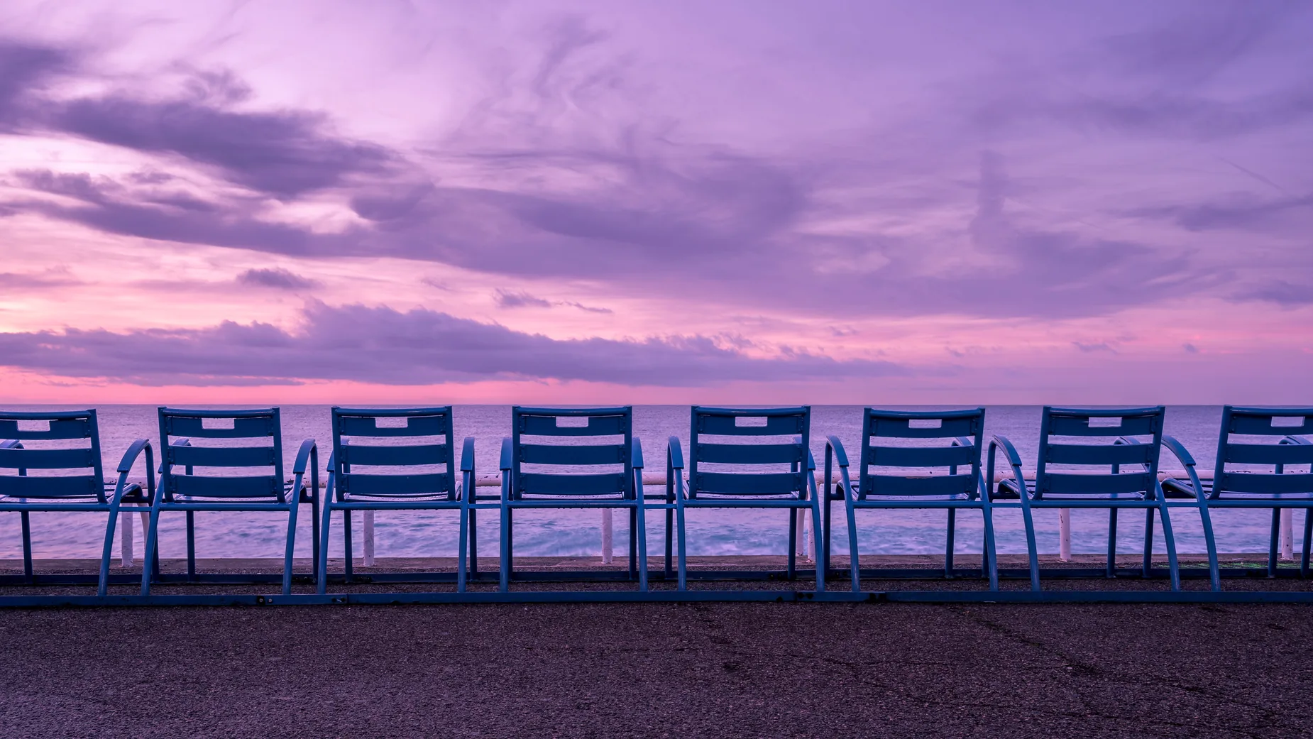 Les chaises bleues de la Promenade des Anglais face à la mer, sous un ciel de coucher de soleil mauve